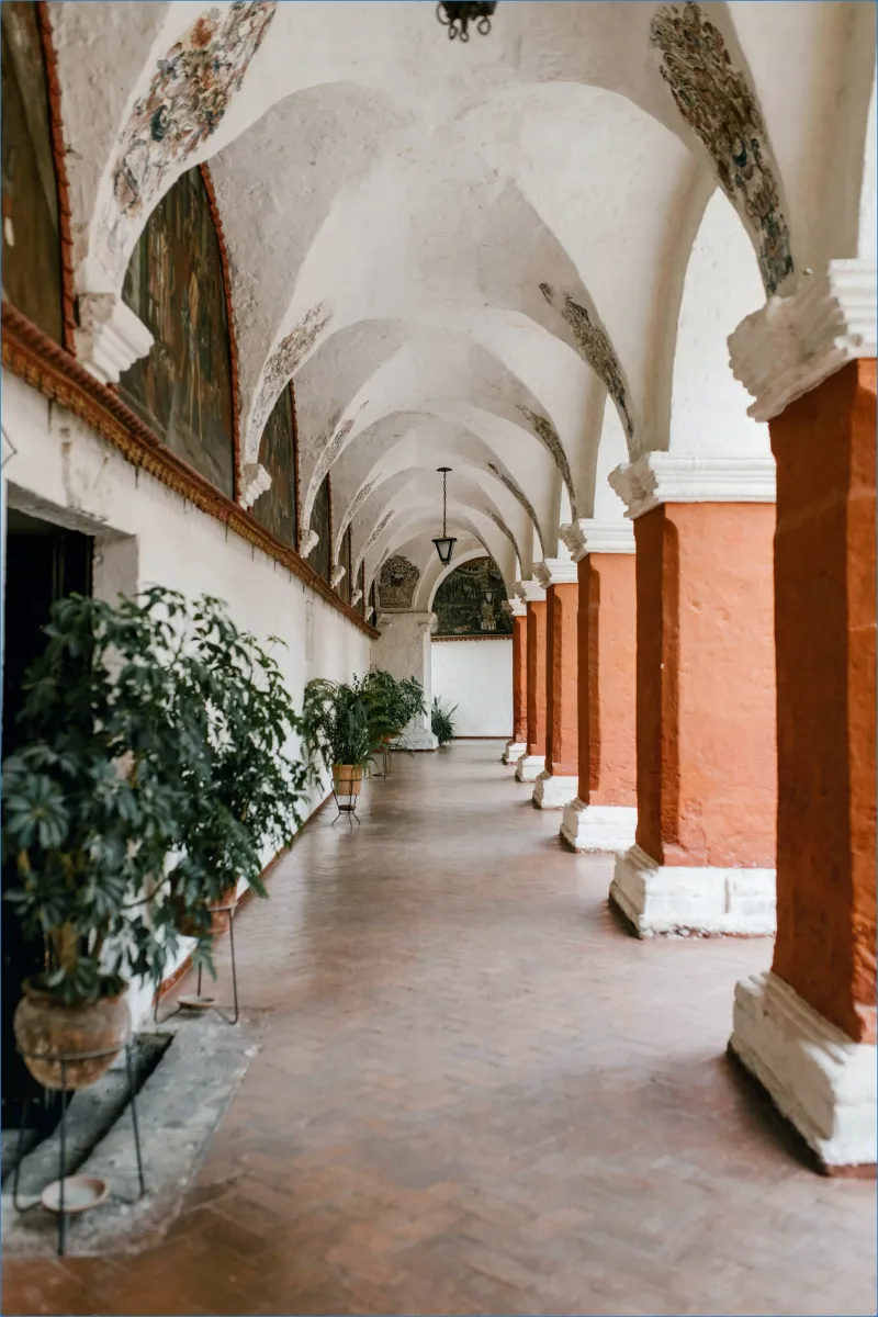 Arched hallway with potted plants and red columns.